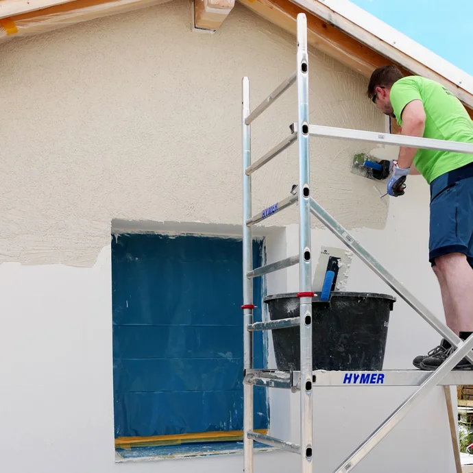 Mann steht auf Arbeitsgerüst und verputzt die Wand mit einer Glättkelle.