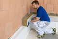 Un bricoleur isole une façade avec de la laine minérale ; étape de l’instruction sur l’isolation extérieure disponible sur le site web de Baumit.