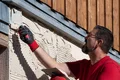 Un homme enduit la façade d’une maison à l’aide d’une truelle, l’air concentré. Travaux de bricolage sur un mur nécessitant une rénovation.