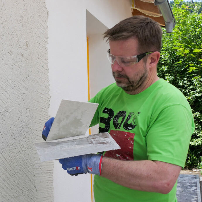 Mann streift Reibebrett an Glättkelle ab, um überschüssiges Bindungsmittel zu entfernen.