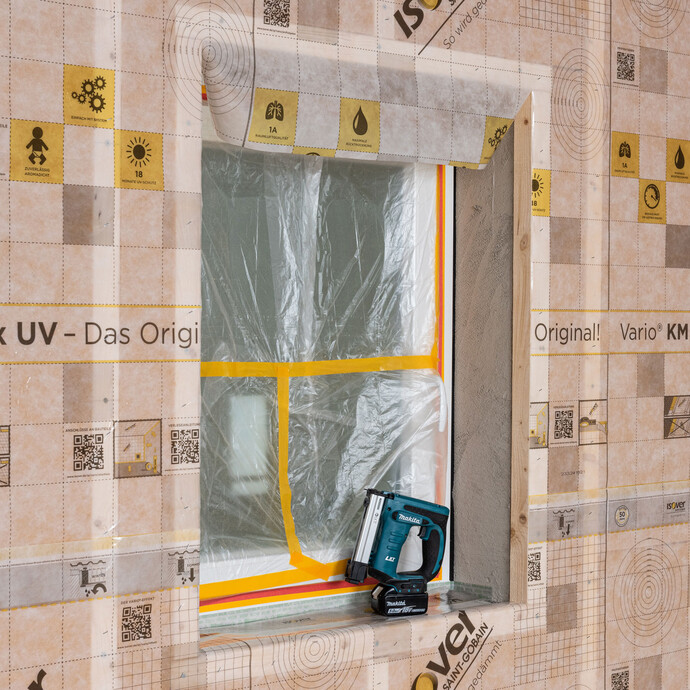 Innendämmung auf Holzkonstruktion: Dampfbremse fachgerecht anbringen. Die überspannte Dampfbremsfolie ist im Bereich des Fensters freigeschnitten. Der Akku-Tacker von Makkita steht auf der Fensterbank.