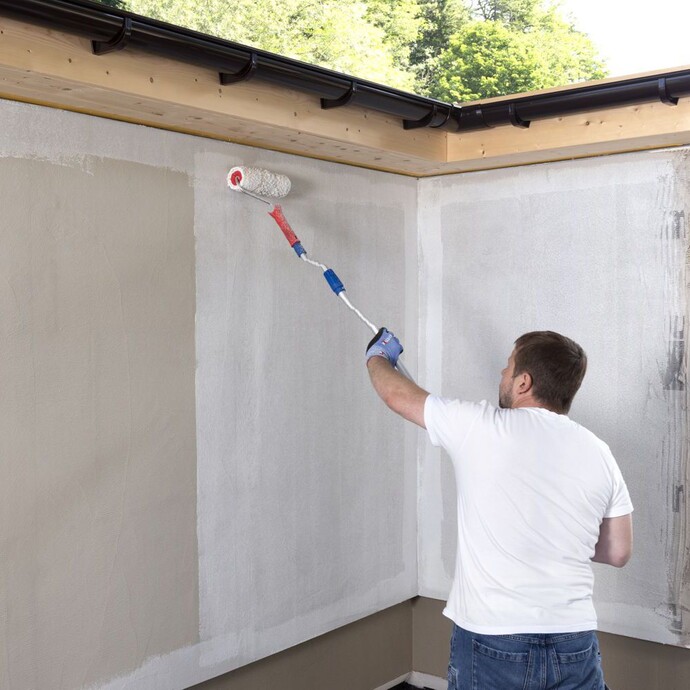 Mann trägt Grundierung großflächig mit einer großen Farbrolle auf der Wand auf.