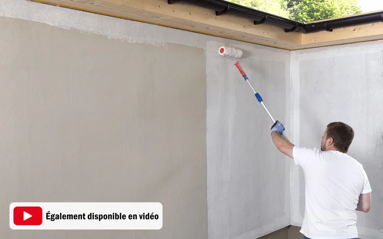 Le bricoleur peint un mur intérieur au rouleau à peinture pour obtenir une finition parfaite. Conseil : appliquer une pression régulière pour un résultat homogène.