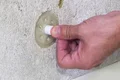 Un pouce enfonce une cheville pour isolant en polystyrène dans la surface murale ; cette étape de la fixation de l’isolant est expliquée.
