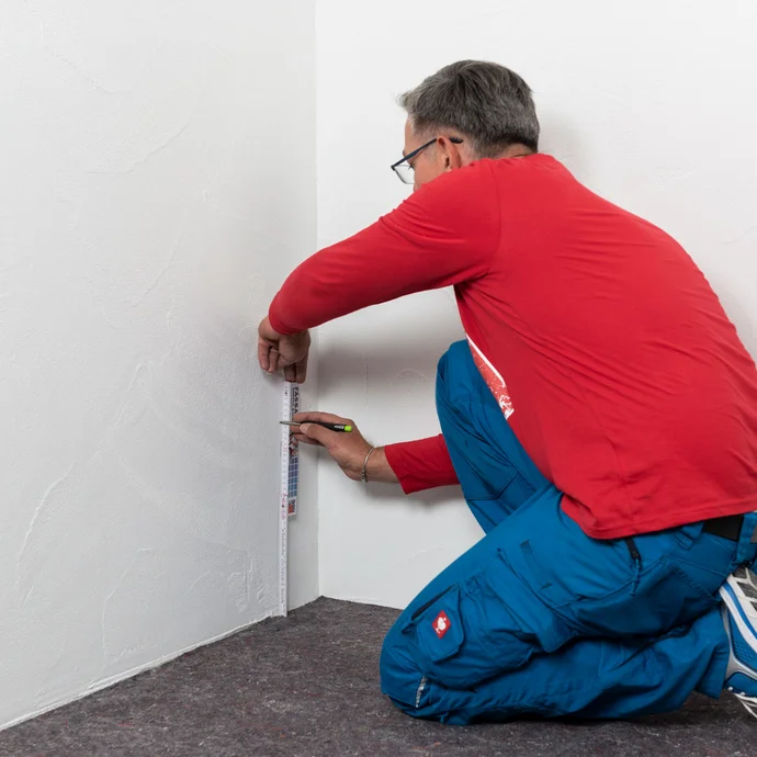 Handwerker misst die Einbauhöhe zur Anbringung der Horizontalabdichtung aus und markiert die Position mit einem Bleistift an der Wand.