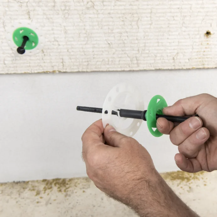Montage d’une cheville pour ITE sur un mur peint en vert pour une isolation thermique efficace.