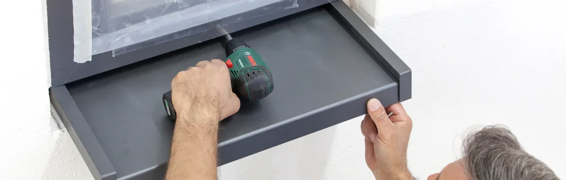 Heimwerker montiert Regal mit Bohrmaschine an Wand.