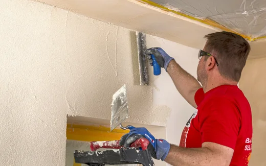 Le bricoleur applique l'enduit de manière uniforme sur le mur ; instructions étape par étape sur Baumit pour une rénovation parfaite.