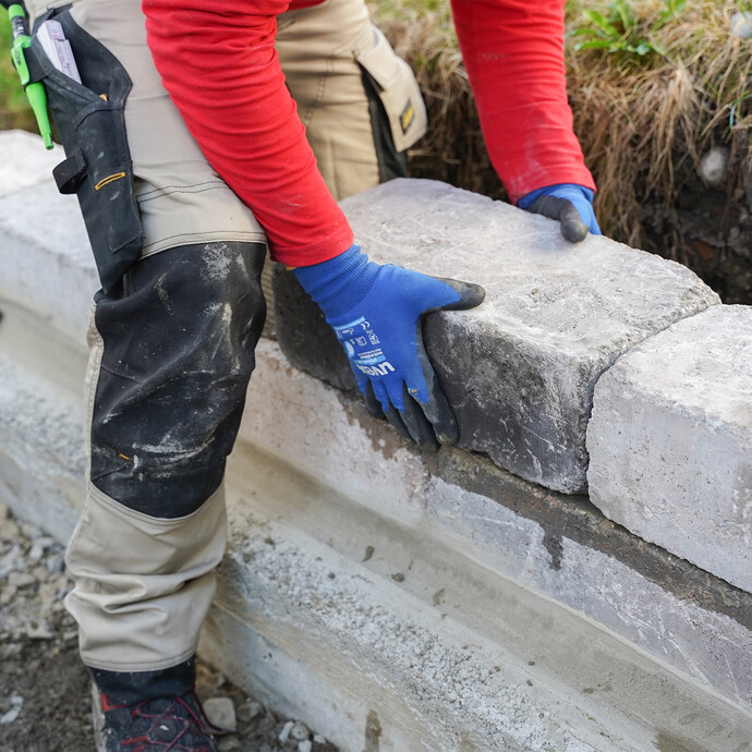 Eine Person positioniert den frisch gesetzten Mauerstein passgenau im Kleberbett. So kann die Gartenmauer fertig gebaut werden.