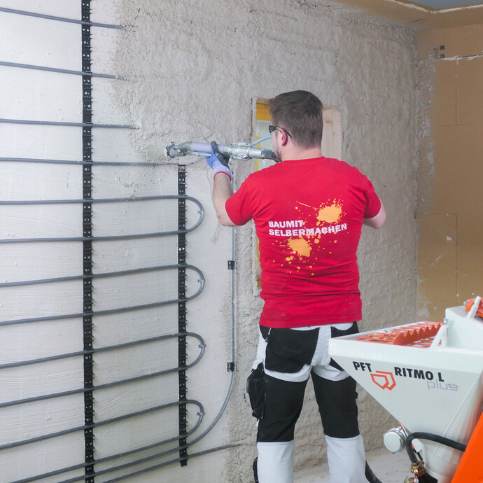 Heimwerker trägt mit einer Putzmaschine mineralischen Putz auf eine Wand mit Wandheizung auf.