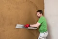 Mann verputzt Innenwand mit Glättkelle, Schritt-für-Schritt-Anleitung für Heimwerker auf Baumit-Selbermachen.