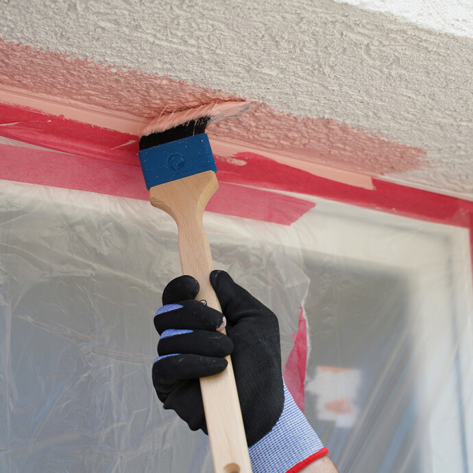 Person streicht Laibung eines Fensters mit einem Pinsel an.