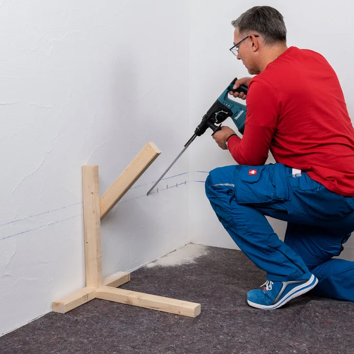 Handwerker bohrt mit einem Winkel von 45 Grad in die markierten Bohrlöcher der ersten Reihe.