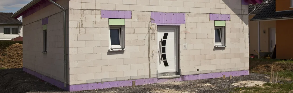 Maison individuelle en gros &oelig;uvre avec des panneaux isolants violets sur la fa&ccedil;ade pour une isolation thermique efficace.