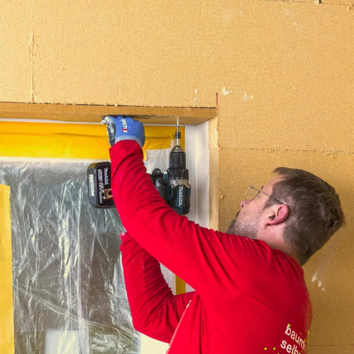 Une personne installe un revêtement de plafond à l'aide d'une visseuse sans fil dans une pièce aux panneaux muraux jaunes.