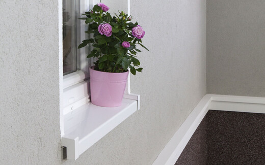 Eine Wand mit grauem Putz über und Mosaikputz unter weißen Stuckelementen. In der Wand ist ein Fenster, es steht ein Blumentopf auf dem Fensterbrett.