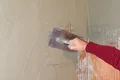 Heimwerker verputzt Wand mit Glättekelle, um glatte Oberfläche zu erzielen. Ideal für Renovierungen und Sanierungsprojekte.
