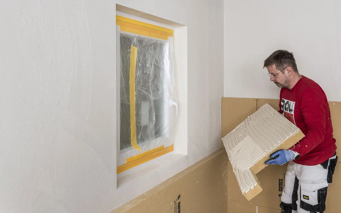 Heimwerker isoliert Wand mit Dämmplatten; Fenster zum Schutz abgeklebt, Schritt-für-Schritt-Dämmtechnik von Baumit.