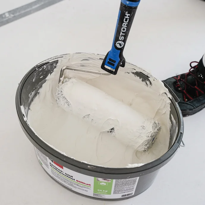 Farbeimer mit weißer Wandfarbe und Farbrolle für Heimwerkerprojekte im Innenausbau.