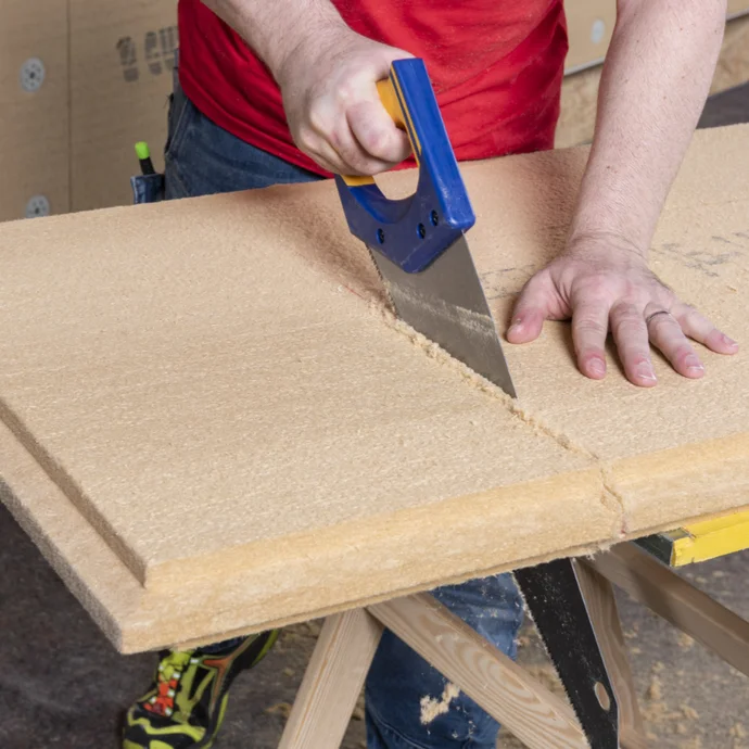 Heimwerker sägt Dämmplatte mit Handsäge auf Holzbockunterlage für Renovierungsprojekt.