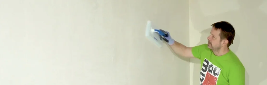 Mann glättet weiße Wand mit Spachtelmasse, DIY-Tipps für glatte Oberflächen.