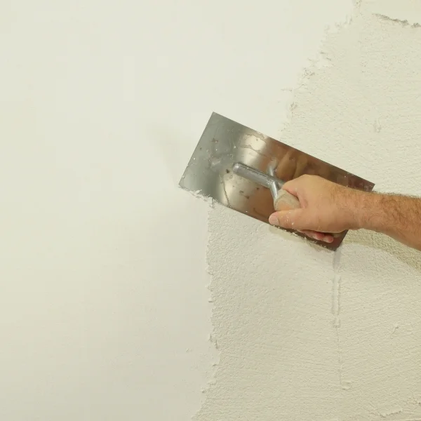 Hand verputzt eine Wand mit einer Kelle für gleichmäßige Oberflächenstruktur.