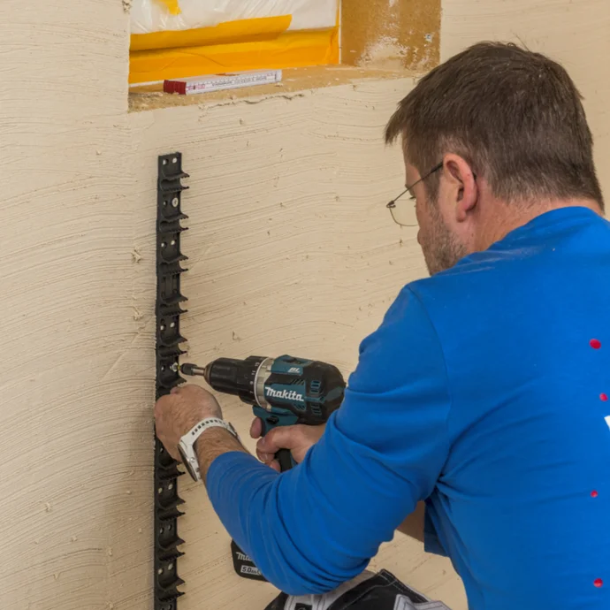 Heimwerker befestigt Führungsschienen für das Verputzen mit Bohrmaschine an einer Wand, Schritt für Schritt Anleitung.