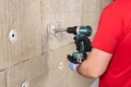 Heimwerker befestigt Dämmplatte mit Akkuschrauber an der Wand.