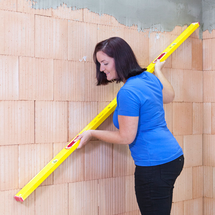 Madame vérifie que le mur ne présente pas d'irrégularités à l'aide d'un long niveau à bulle.