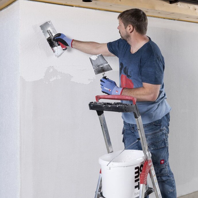 Person steht auf Leiter und trägt Strukturputz mit einer Glättkelle an einer Wand auf.