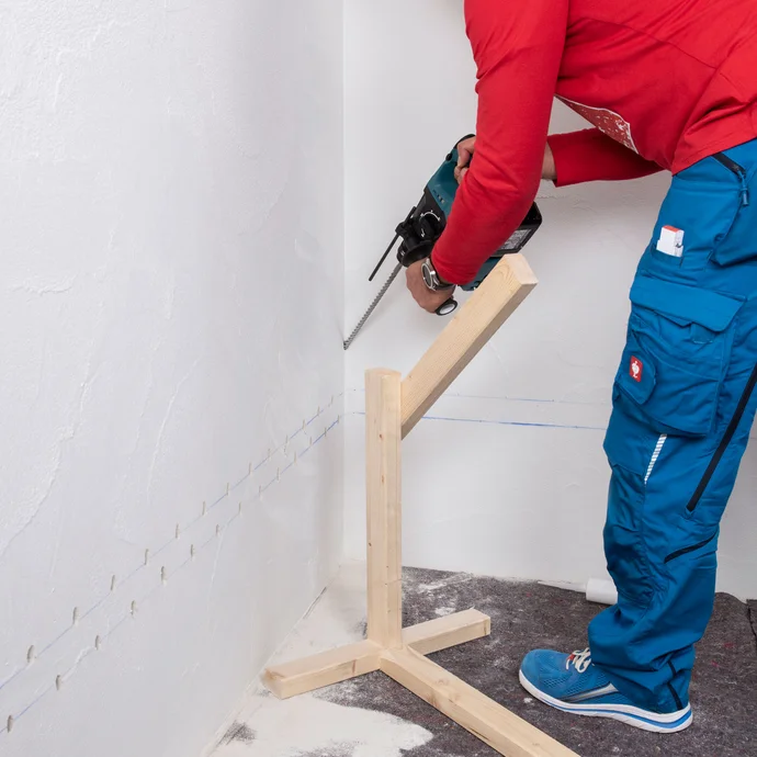 Handwerker bohrt in den markierten Bohrlochpunkt in der Innenecke der Wand.