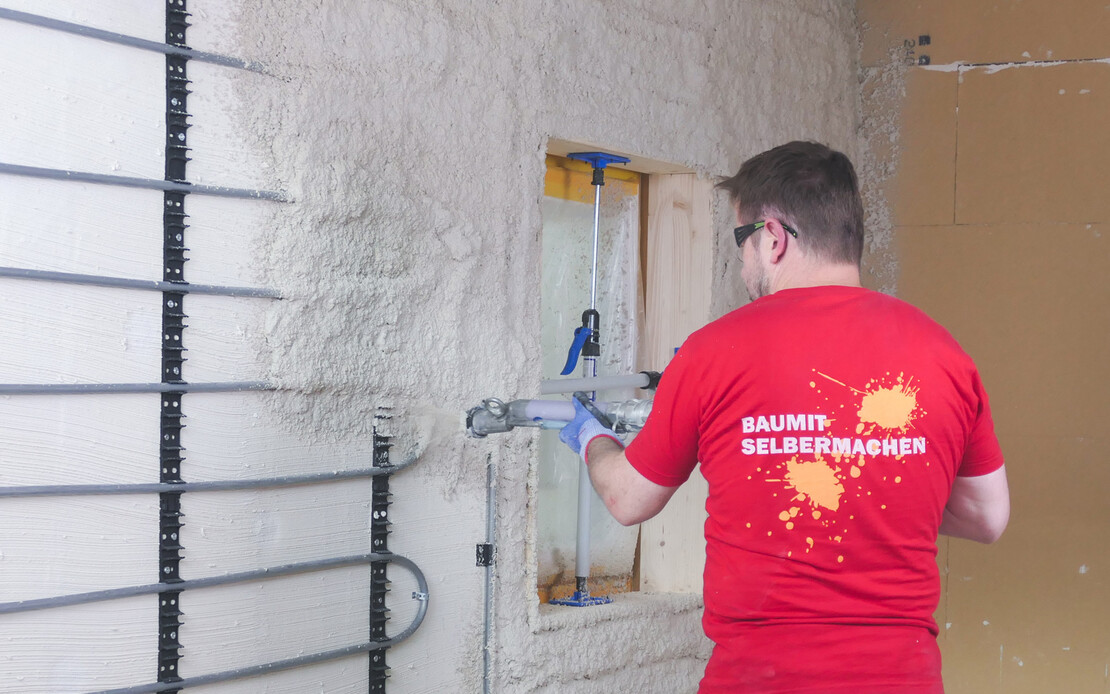 Putz wird von Heimwerker mit Putzmaschine auf eine Wand mit einer wassergeführten Wandheizung (Heizschlangen) aufgetragen.