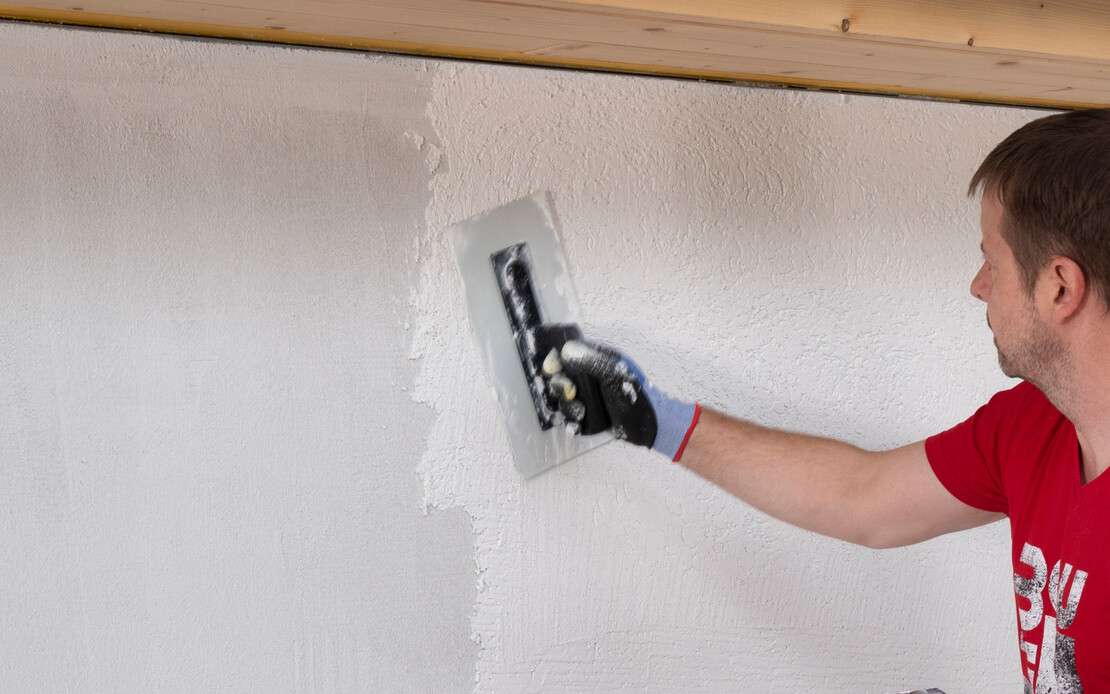 Mann verputzt eine Wand mit wei&szlig;em Silikonharzputz.