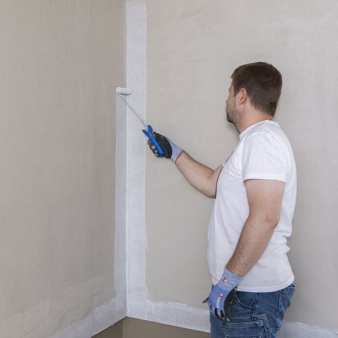 Person trägt Grundierung an der Innenecke einer Wand mit einer kleinen Farbrolle auf.