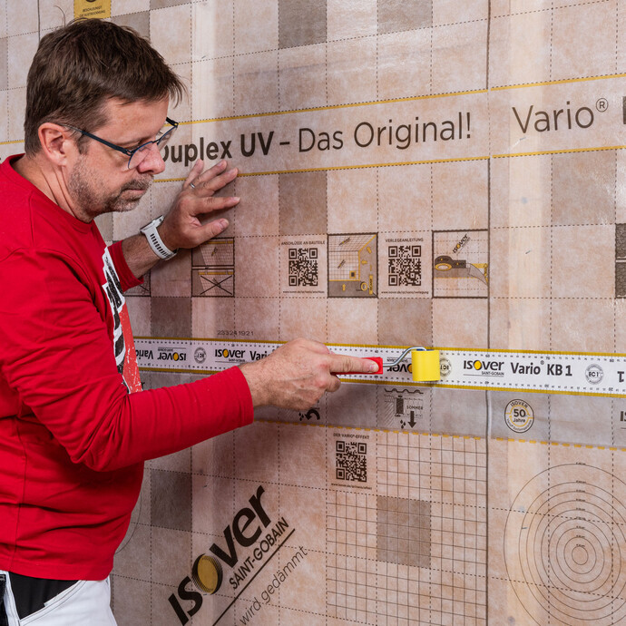 Baumit Handwerker drückt das Folienklebbeband ISOVER Vario KB1 mit einer Andruckwalz vollflächig und ohne Falten oder Blasen fest an. Baumit Anleitung zum Selbermachen - Dampfbremse bei einer Innendämmung mit Tragkonstruktion einbauen.