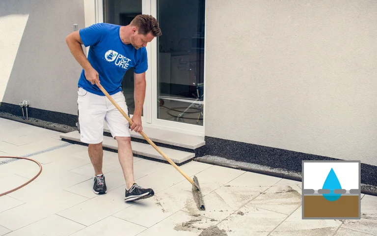 Heimwerker fegt überschüssigen Mörtel von frisch verlegten Terrassenplatten zu entfernen.