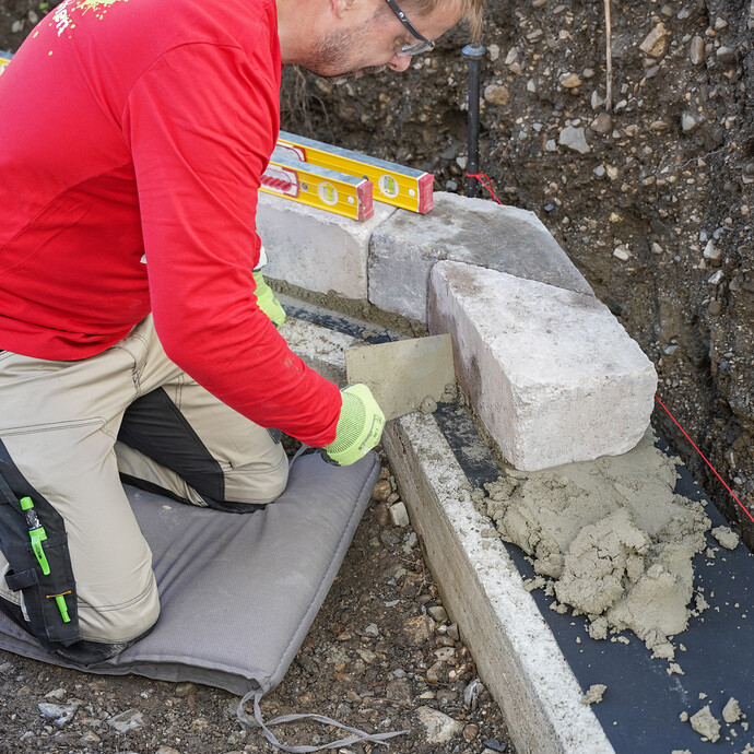 Mit einer Maurerkelle wird überschüssiger Mörtel nach dem Setzen der Steine entfernt.
