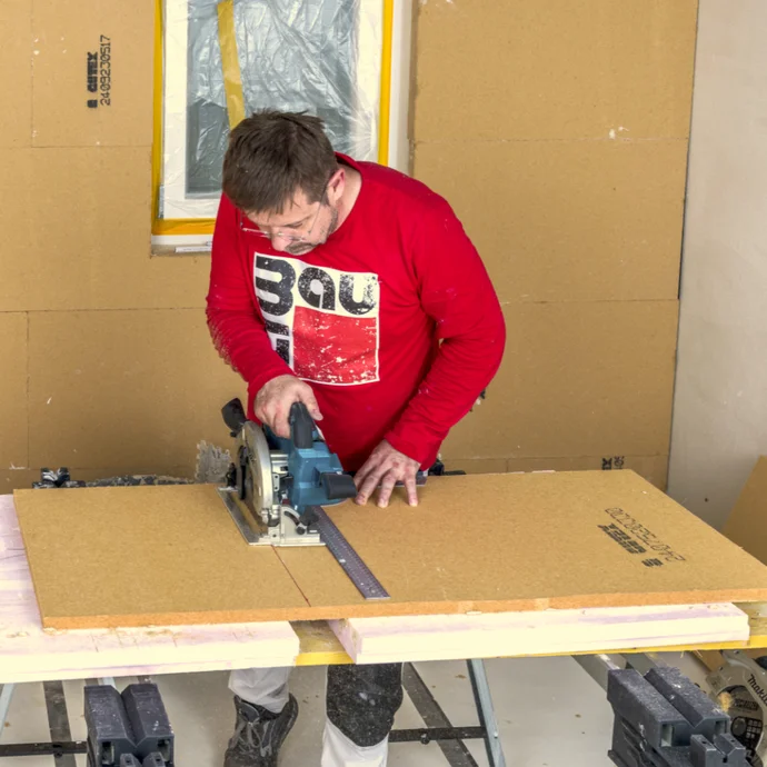 Un bricoleur découpe un panneau de particules à l’aide d’une scie circulaire pour l’aménagement intérieur ; utilisation de produits Baumit.