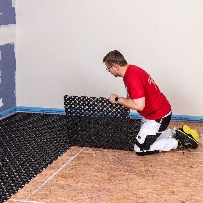 Heimwerker verlegt auf dem Boden die Noppenbahnen überlappt für die wassergeführte Fußbodenheizung.