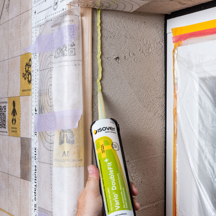 Die Vario DoubleFit+ Klebe-Dichtmasse von ISOVER wird auf der Laibung aufgetragen, um das Folienstück Dampfbremse anzukleben.