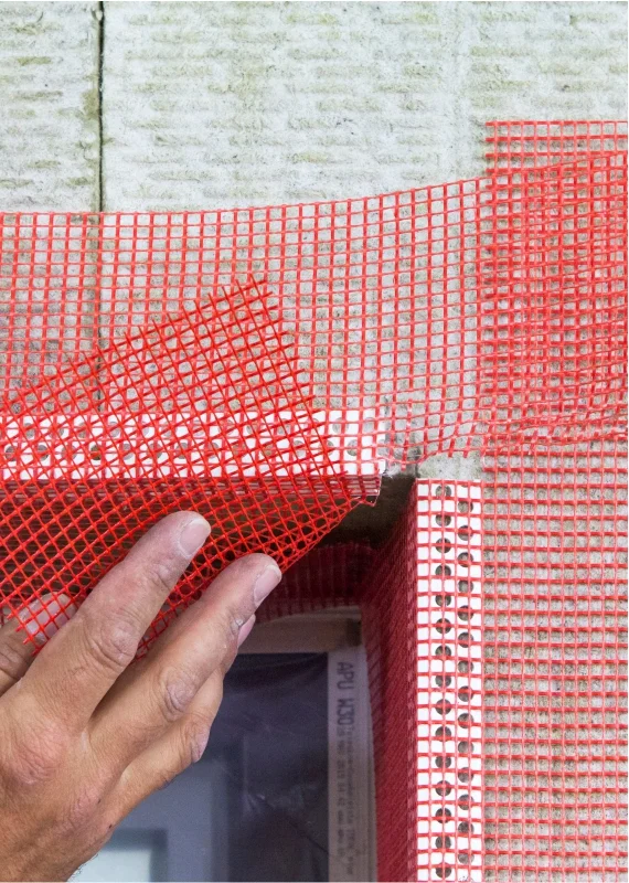 Renforcement de l'isolant de façade à l'aide d'un treillis d’armature rouge sur un angle de bâtiment.