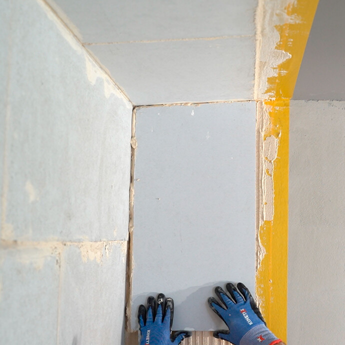 Heimwerker setzt den Kalziumsilikatplatte Anschlusskeil vorsichtig in den frisch aufgetrgenen Putz. Der Keil stößt bündig an die geklebte Platte an der Wand und Decke.