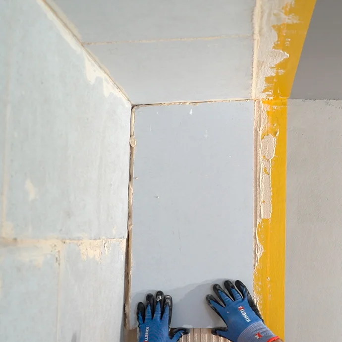 Heimwerker setzt den Kalziumsilikatplatte Anschlusskeil vorsichtig in den frisch aufgetrgenen Putz. Der Keil stößt bündig an die geklebte Platte an der Wand und Decke.
