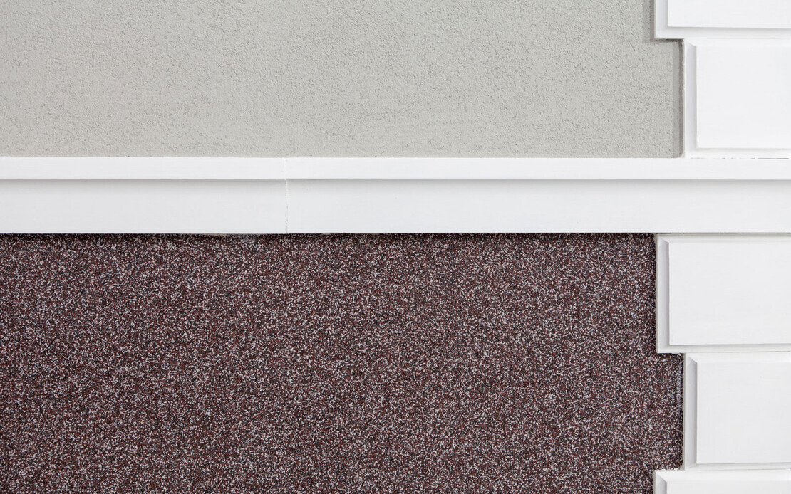 Nahaufnahme von wei&szlig;en Stuckprofilen mit Mosaikputz unterhalb und grauem Putz oberhalb der Stuckelemente.