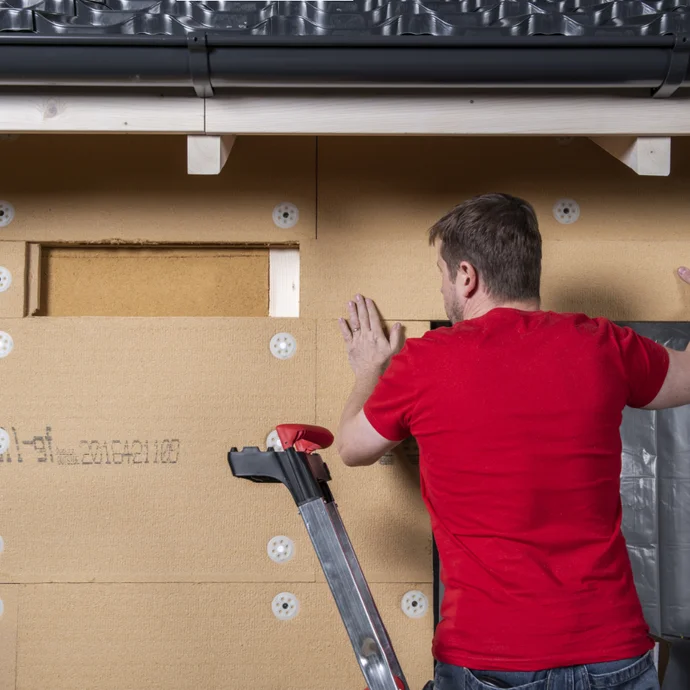 Heimwerker isoliert Hausfassade mit Dämmplatten; Leiter als Unterstützung.
