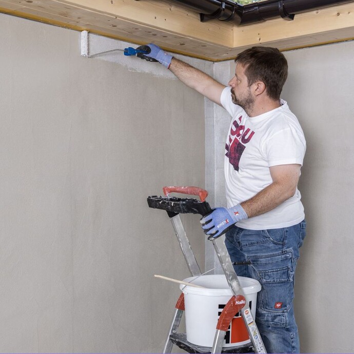 Mann steht auf Leiter und trägt Grundierung an Wandränder mit einer kleinen Farbrolle auf.