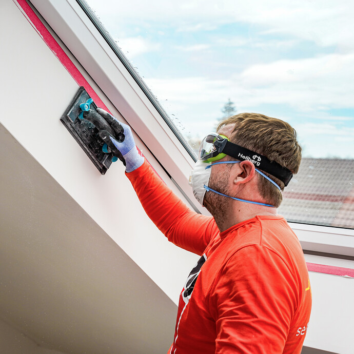 L'embrasure de la fenêtre de toit est poncée à l'aide d'une ponceuse manuelle.