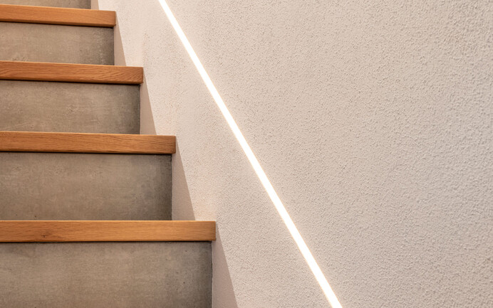 Escalier moderne dans une maison individuelle en béton et bois avec éclairage indirect et InStyle Edelweiss fin blanc brillant.