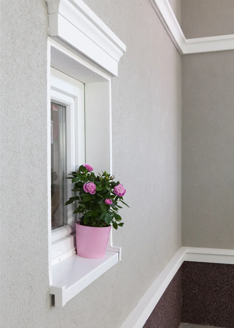 Fensterbank mit rosafarbenem Blumentopf vor frisch renovierter, beiger Putzfassade. Ideal für Heimwerkerprojekte.