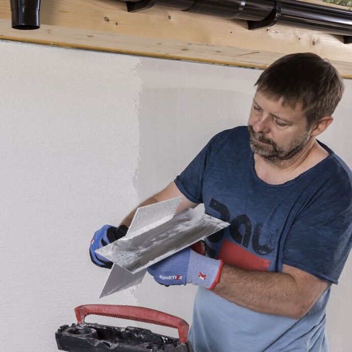 Mann streift Reibebrett an der Glättkelle ab, um überflüssiges Bindemittel zu entfernen.